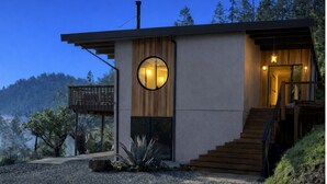 A modern house with a circular window, a wooden deck, and a staircase leading to the entrance. - Epic views, modern luxury, private retreat in West Marin on hilltop 2 acre (Lagunitas-Forest Knolls)