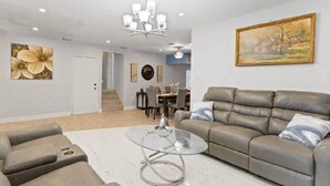 Una sala moderna con un sofá de cuero, una mesa de centro de vidrio y una zona de comedor con una escalera.
