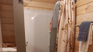 A wooden-paneled bathroom with a shower, toilet, and a shelf with towels. - Buffalo Camp #7 (East Glacier Park)