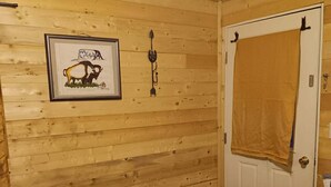 A wooden-paneled room with a bed, a framed picture, a door with a towel, and a vent. - Buffalo Camp #7 (East Glacier Park)