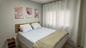 Een slaapkamer met een bed, een nachtkastje, een plafondlamp en drie kunstwerken aan de muur.