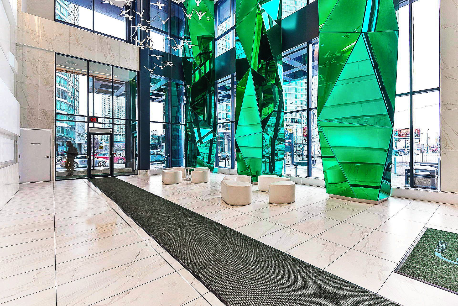 A modern lobby with a glass entrance, green structural elements, and seating areas.