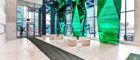 A modern lobby with a glass entrance, green structural elements, and seating areas.