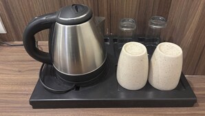 Ein Edelstahl-Wasserkocher auf einer schwarzen Ablagefläche, daneben zwei tassen mit Punktmuster.