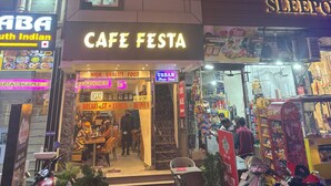 Ein mehrgeschossiges Gebäude, im Erdgeschoss leuchtet ein Schild mit der Aufschrift 'CAFE FESTA'.