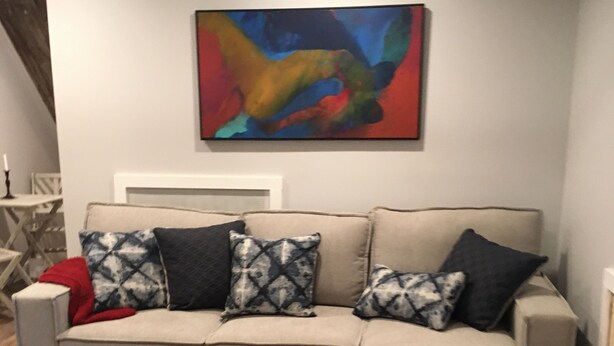 A sectional sofa with patterned cushions, a colorful abstract painting above it, and a wooden floor. - Charming 1-bedroom apartment with AC in peaceful Nyack (Nyack)