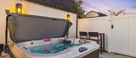 Un bain à remous équipé d’un panneau de commande, ainsi qu’une table et des chaises, le tout installé dans un jardin.