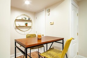 A dining area with a wooden table and chairs, a round gold-framed shelf with decorative items, and a door with a handle. - Stay Cozy in CoHi DC (Washington DC)