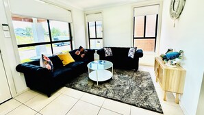 Ein Wohnzimmer mit einem schwarzen Sofa, einem runden Glastisch und einem kleinen Holznachttisch mit einer Dekoration.