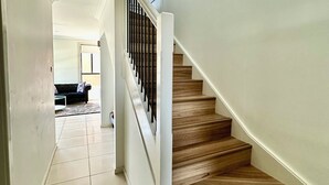 Eine Treppe mit Holzdielen und einem weißen Geländer, die zu einem Wohnbereich mit einer Couch und einem Couchtisch führt.
