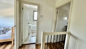 Ein Flur mit Holzboden, einem Bett mit gestreifter Bettdecke und Blick in einen Küchenbereich mit Spüle und Kühlschrank.