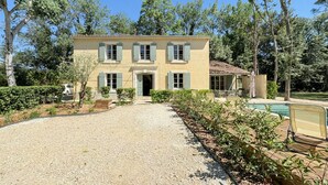 Un edificio a due piani con vialetto sterrato, piscina e giardino.