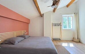 Een slaapkamer met een bed, een plafondventilator, een raam met gordijnen en een kledingrek.