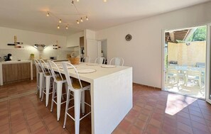 Een moderne keuken met witte kasten, een eethoek met witte stoelen, en een grote schuifglazen deur die leidt naar een terras.