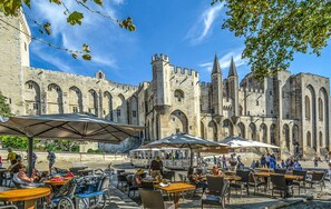 Een historisch gebouw met boogvensters en torens, omringd door terrassen met parasols.
