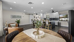 A modern kitchen with white cabinets, a black refrigerator, and a dining area with a wooden table and chairs. - Palm Blanc- Modern Retreat • Pool • Firepit (West Palm Beach)