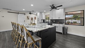 A modern kitchen with a large island, white cabinets, and a black countertop. - Palm Blanc- Modern Retreat • Pool • Firepit (West Palm Beach)