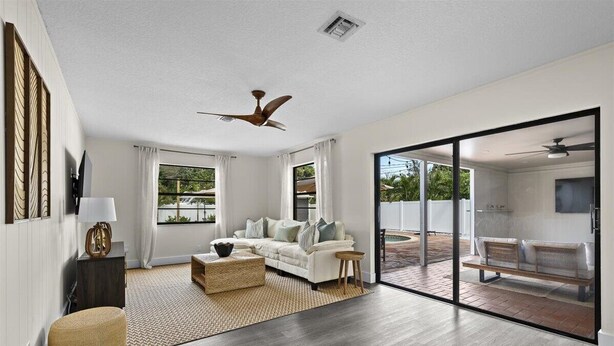 A spacious living room with a white sofa, a coffee table, and a large sliding glass door leading to an outdoor area. - Palm Blanc- Modern Retreat • Pool • Firepit (West Palm Beach)