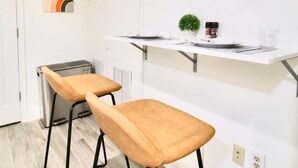 A modern kitchen with two bar stools, a white countertop, and a small potted plant. - Studio Not Far from Capitol Hill, Walk to METRO (Washington)