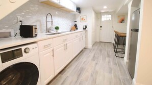 A modern kitchen with white cabinets, a built-in washing machine, and a bar area with stools. - Studio Not Far from Capitol Hill, Walk to METRO (Washington)