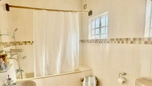 A bathroom with a bathtub, a sink, a toilet, and a window. - Experience comfort & luxury in this stylish villa  in Area 10, lilongwe (Lilongwe)