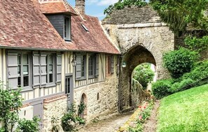 Une maison traditionnelle à colombages, dotée d’un arc en pierre et d’un étroit sentier menant à l’entrée.