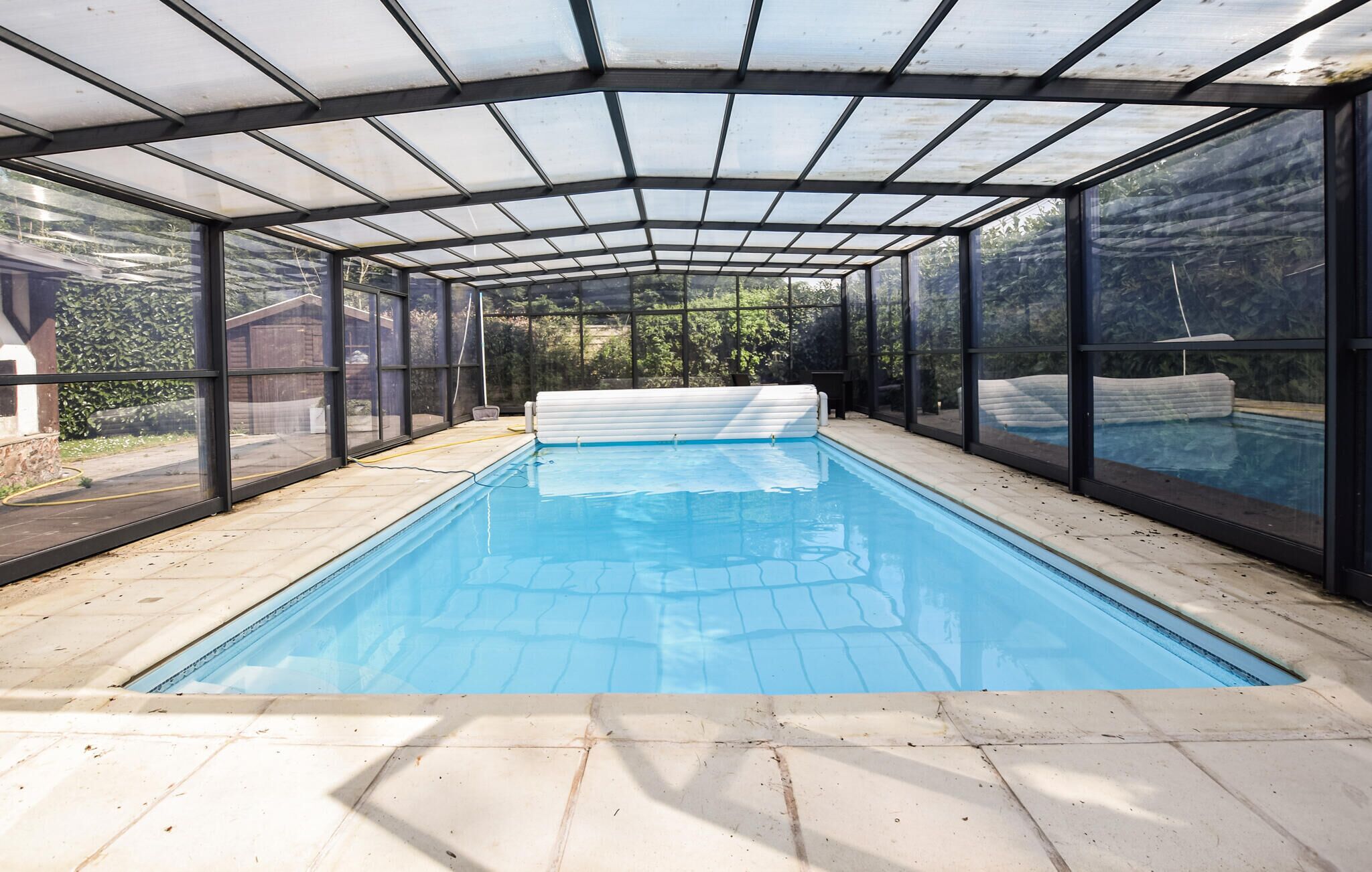 An indoor swimming pool with a glass enclosure, clear blue water, and a tiled floor.