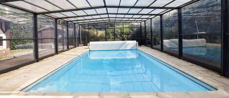 An indoor swimming pool with a glass enclosure, clear blue water, and a tiled floor.