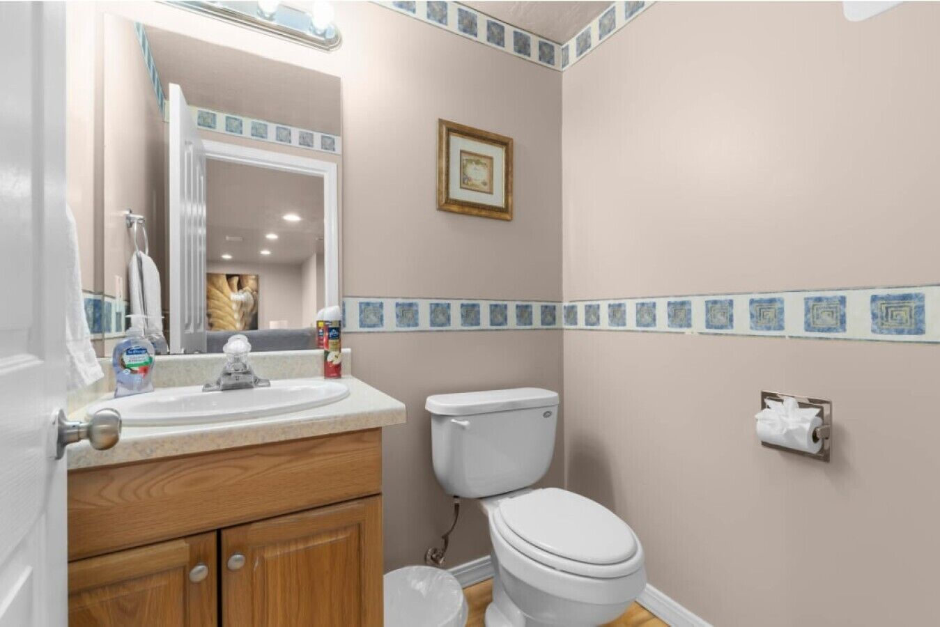 Une salle de bain avec un meuble-lavabo en bois, des toilettes blanches, un miroir et un tableau encadré au mur.