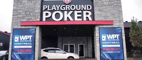 A building with a sign that reads "PLAYGROUND POKER." There are two large posters on either side of the entrance advertising the World Poker Tour in Montreal with dates and prize money.
