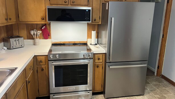 A kitchen with wooden cabinets, a stainless steel refrigerator, a microwave, a toaster, and an oven. - 2br Albany Corporate Comfort (Albany)