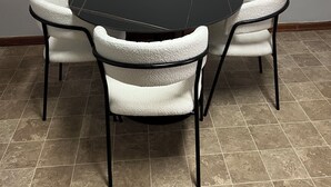 A round table with a black top surrounded by four white cushioned chairs with black frames. - 2br Albany Corporate Comfort (Albany)