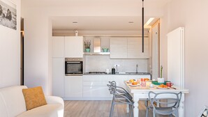 Une cuisine moderne avec des meubles blancs, une table à manger avec des chaises et un canapé avec un coussin.