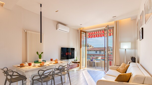 Un salon moderne comprenant un canapé, une table à manger avec des chaises, un téléviseur et une vue sur l’extérieur, visible à travers une porte vitrée.