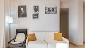 Un salon moderne avec un canapé blanc, un fauteuil foncé et une lampe sur pied. Trois tableaux encadrés ornent le mur.