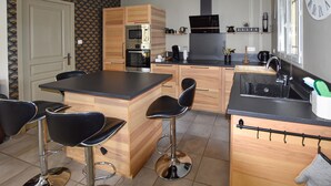 A compact kitchen with wooden cabinets, a central island with bar stools, a built-in oven, and a coffee machine. - Maison avec piscine privée (Mazan)