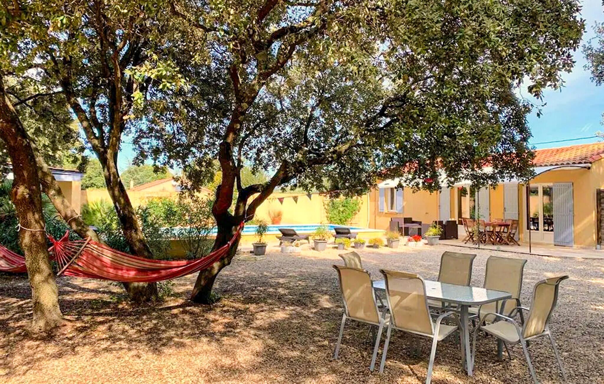A patio with a table and chairs, a hammock, and a pool in the background.