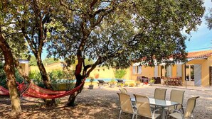 A patio with a table and chairs, a hammock, and a pool in the background. - Maison avec piscine privée (Mazan)