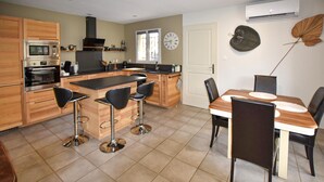 A modern kitchen with a central island, bar stools, a dining table with chairs, and an air conditioning unit on the wall. - Maison avec piscine privée (Mazan)