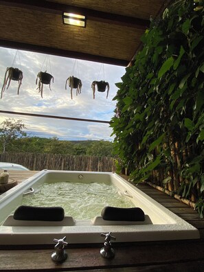 Un bain à remous doté de deux robinets, entouré d’une clôture en bambou et d’une végétation luxuriante.