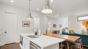 Een moderne keuken met een centraal kookeiland, roestvrijstalen apparatuur en hanglampen.