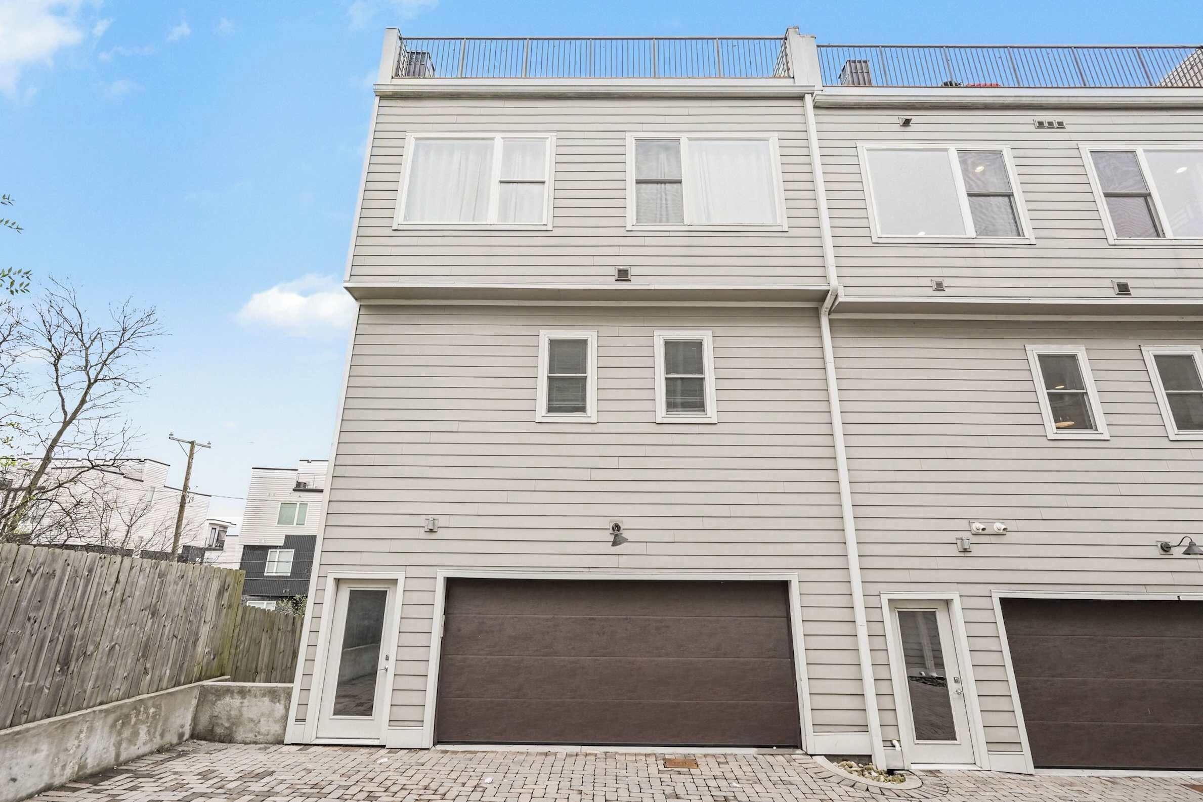 A two-story building with a garage, a wooden fence, and a clear sky.