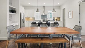 Een moderne keuken met witte kasten, een houten eettafel en zwarte metalen stoelen.