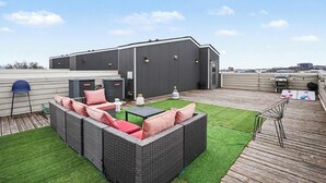 Eine Dachterrasse mit Rattanmöbeln, einem kleinen Tisch und einem Grillbereich.