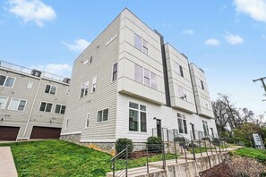 A modern multi-story residential building with a flat roof, large windows, and a visible garage. - Rooftop Views | Sleeps 12 | 10 Min to Broadway (Nashville)