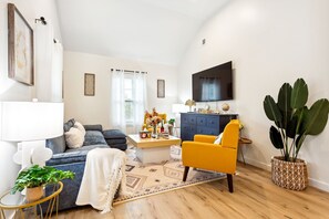 Ein modernes Wohnzimmer mit einer Couch, einem gelben Sessel, einem Couchtisch und einem an der Wand montierten Fernseher.