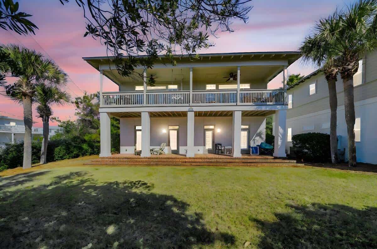 A two-story house with a balcony, surrounded by palm trees and a grassy yard.