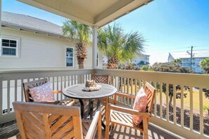 A covered outdoor seating area with a table and chairs, palm trees, and a view of a residential building. - Resting Beach Place by Stay on 30a (Seacrest Beach)