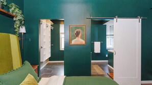 Een kamer met een bed, een groene bank, een schilderij aan de muur en een deur naar een andere kamer.