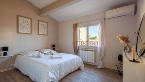 A bedroom with a large bed, a window with curtains, a radiator, and framed artwork on the wall. - Maison Flammarion - Welkeys (Avignon)